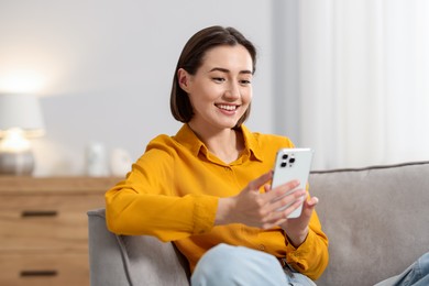 Photo of Woman using modern smartphone in armchair at home