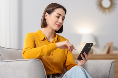 Photo of Woman using modern smartphone in armchair at home