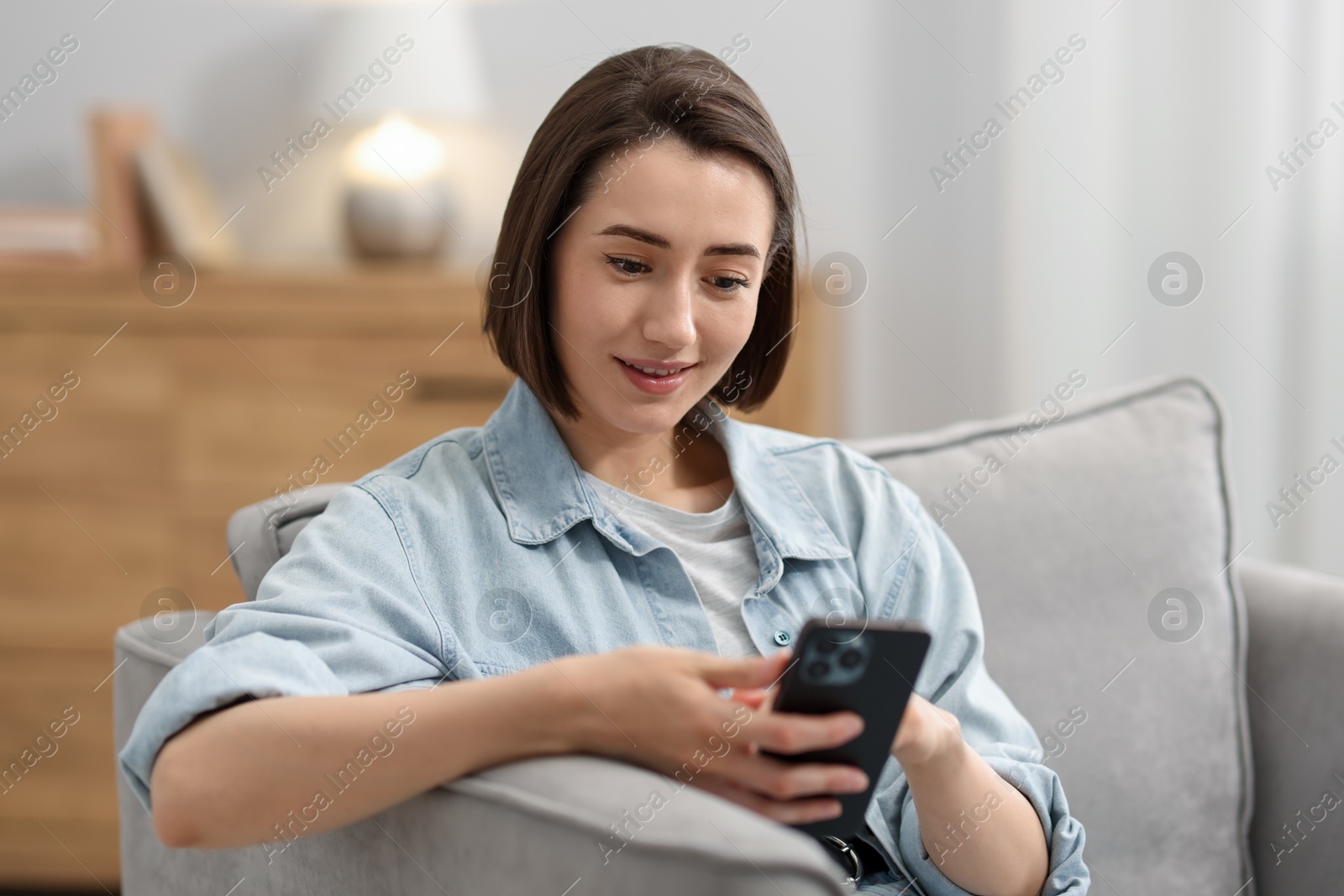 Woman using modern smartphone in armchair at home Photo of Woman using modern smartphone in armchair at home