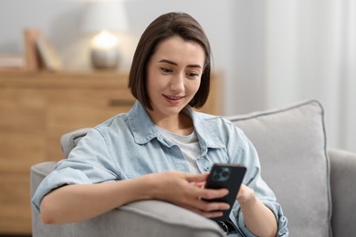 Photo of Woman using modern smartphone in armchair at home