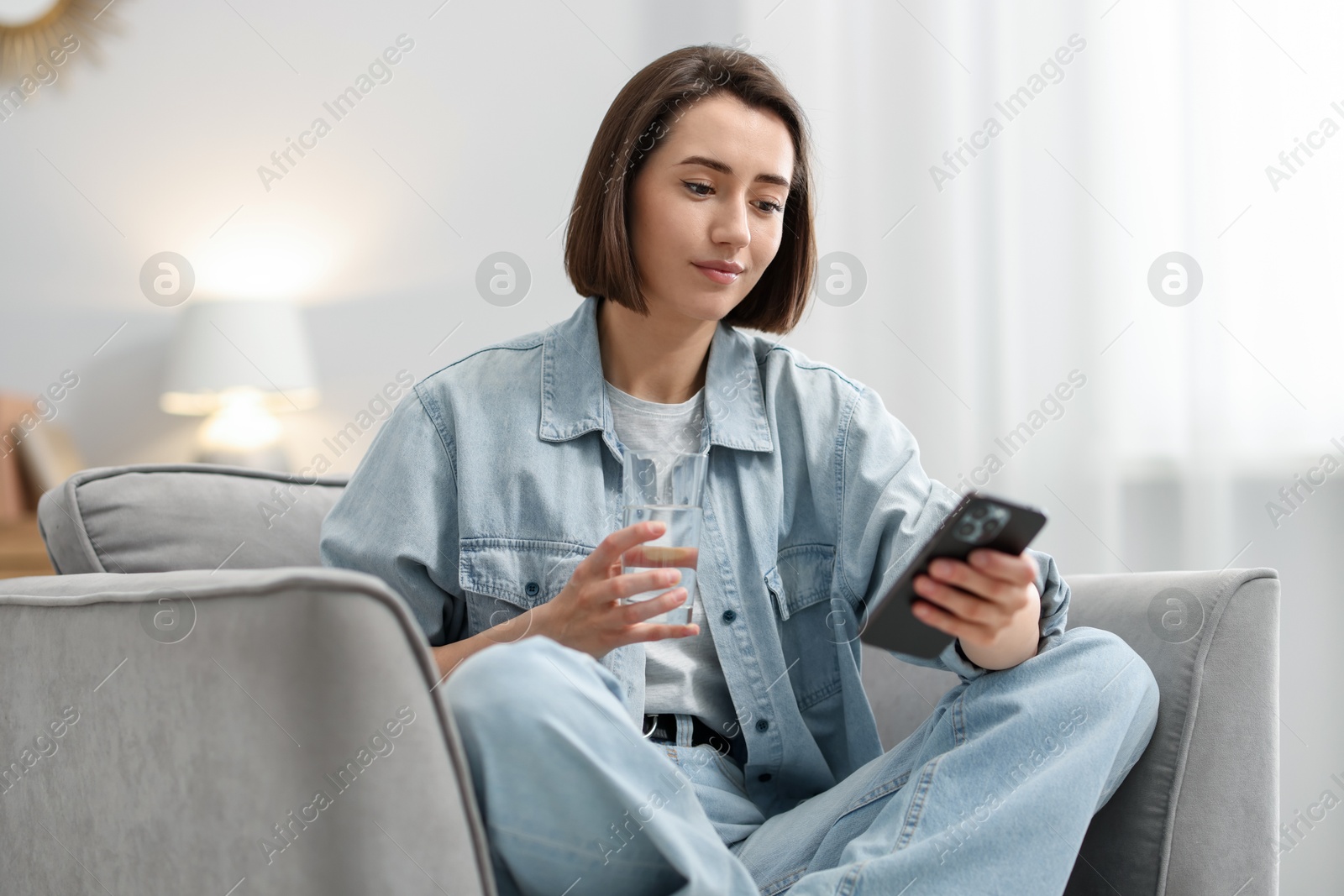 Woman using modern smartphone in armchair at home Photo of Woman using modern smartphone in armchair at home