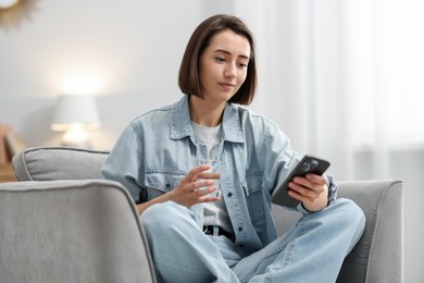 Photo of Woman using modern smartphone in armchair at home