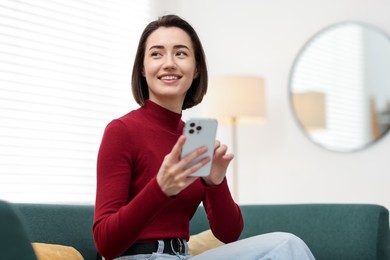 Photo of Woman using modern smartphone on sofa at home