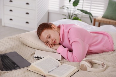 Photo of Tired teenage student sleeping near books and laptop on bed at home