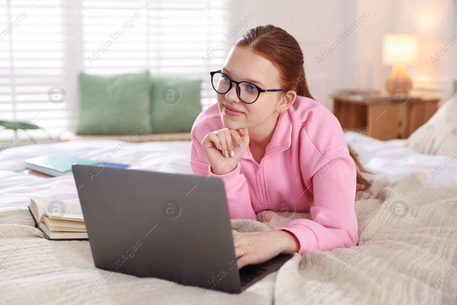 Teenage student in glasses using laptop while studying on bed at home Photo of Teenage student in glasses using laptop while studying on bed at home