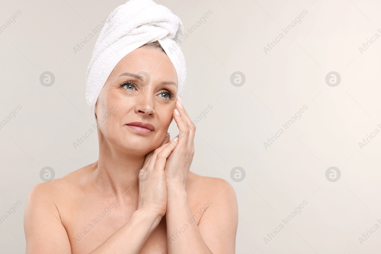 Beautiful woman with towel wrapped on her head against light background. Space for text Photo of Beautiful woman with towel wrapped on her head against light background. Space for text