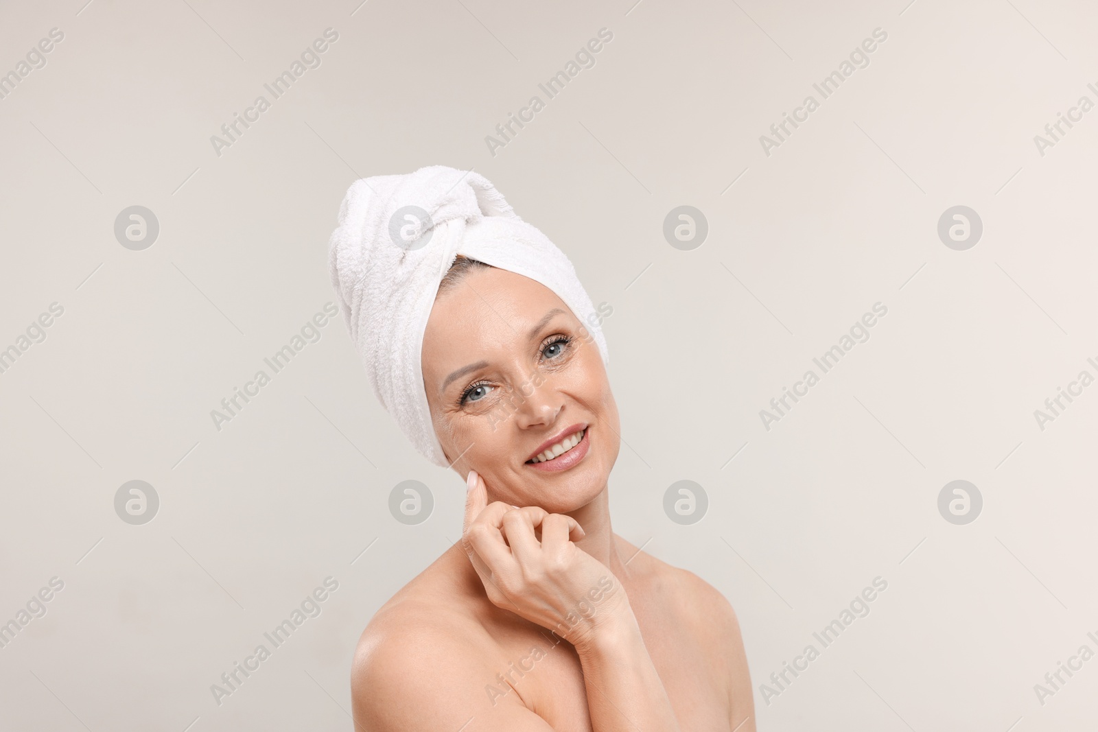 Beautiful woman with towel wrapped on her head against light background Photo of Beautiful woman with towel wrapped on her head against light background