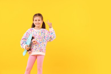 Photo of Little girl with penny board showing V sign on yellow background, space for text
