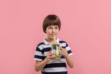 Photo of Cute little boy drinking lemonade on pink background. Refreshing drink