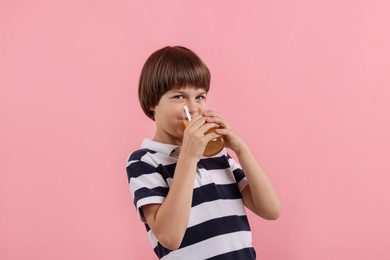 Photo of Cute little boy drinking orange juice on pink background. Refreshing drink