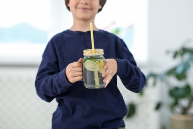 Photo of Little boy with mason jar of lemonade at home, selective focus. Refreshing drink