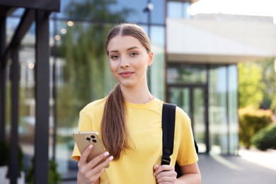 Photo of Teenage girl with smartphone and backpack outdoors