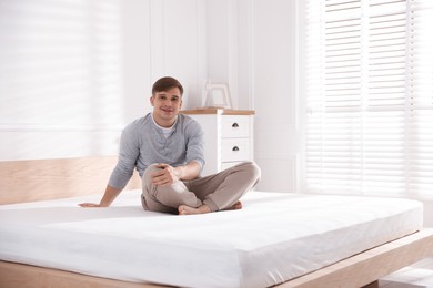 Photo of Young man sitting on bed with soft mattress at home