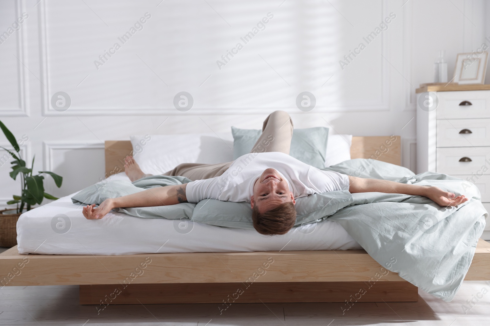 Young man lying on bed with soft mattress at home Photo of Young man lying on bed with soft mattress at home