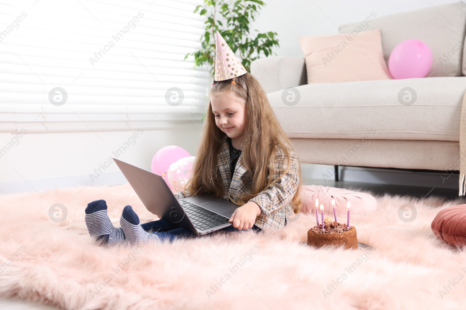 Photo of Birthday celebration. Little girl with cake having video call via laptop at home