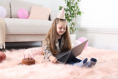 Photo of Birthday celebration. Little girl with cake having video call via laptop at home
