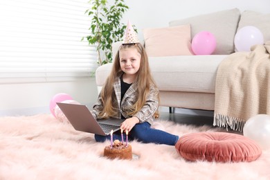 Photo of Birthday celebration. Little girl with cake having video call via laptop at home