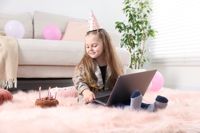 Photo of Birthday celebration. Little girl with cake having video call via laptop at home