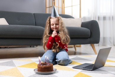 Photo of Birthday celebration. Little girl with cake having video call via laptop at home