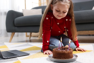 Photo of Birthday celebration. Little girl with cake having video call via laptop at home