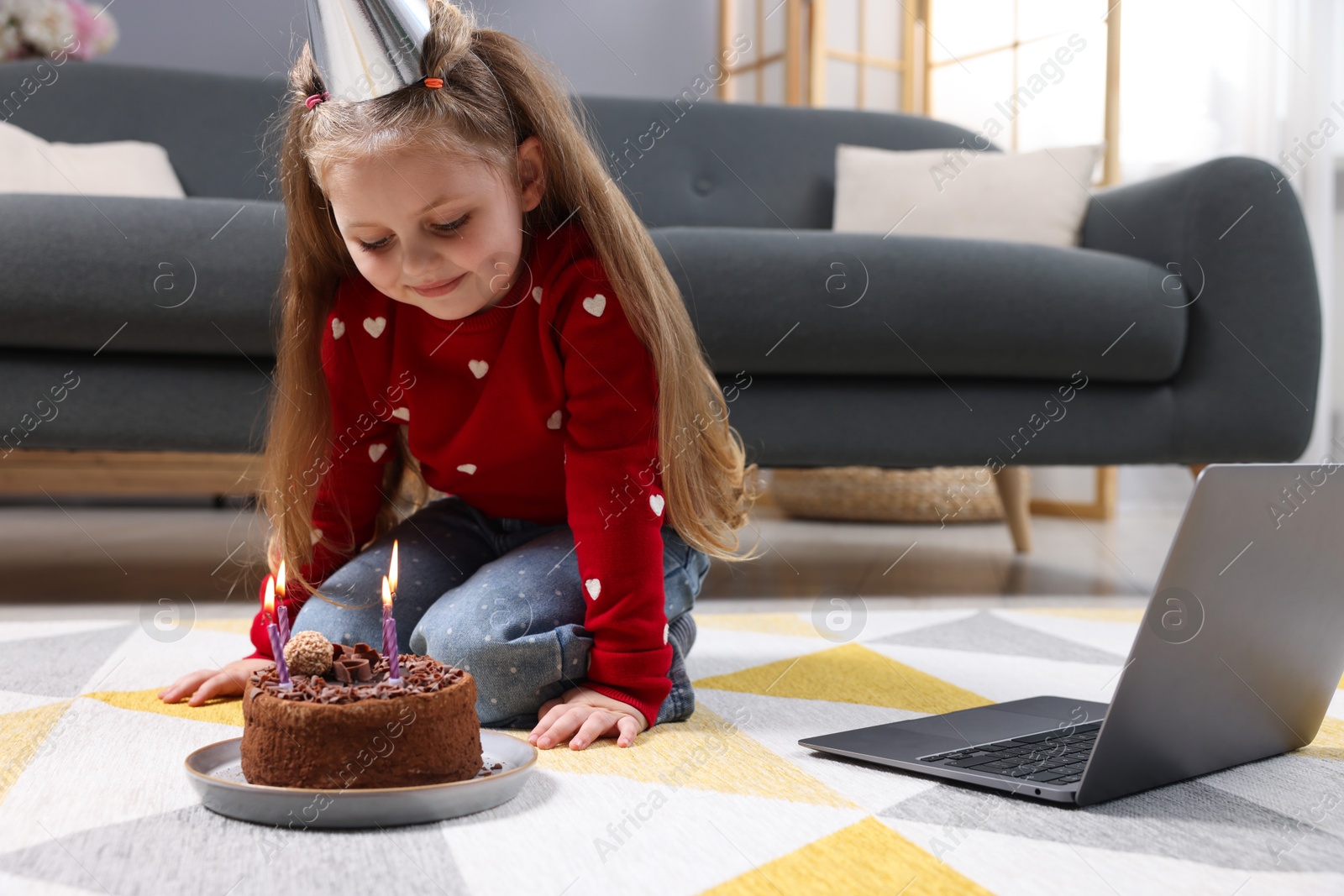 Photo of Birthday celebration. Little girl with cake having video call via laptop at home