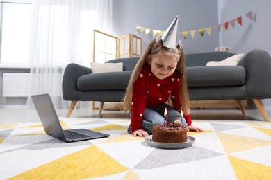 Photo of Birthday celebration. Little girl with cake having video call via laptop at home