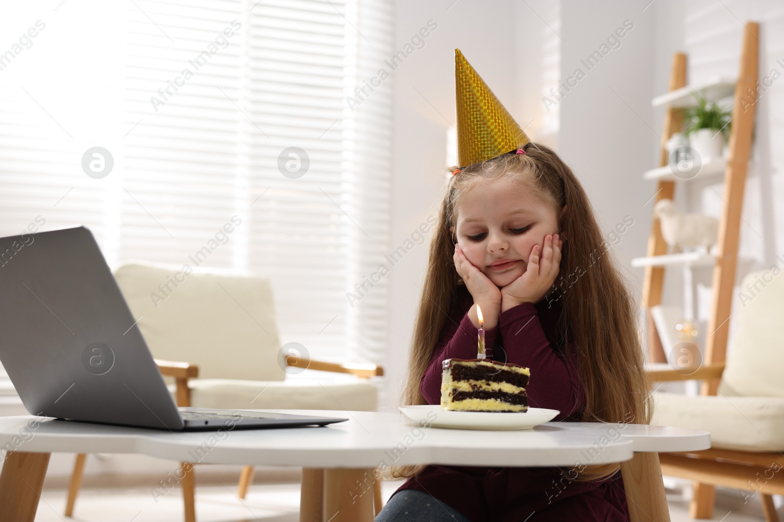 Birthday celebration. Little girl with piece of cake having video call via laptop at table indoors Photo of Birthday celebration. Little girl with piece of cake having video call via laptop at table indoors