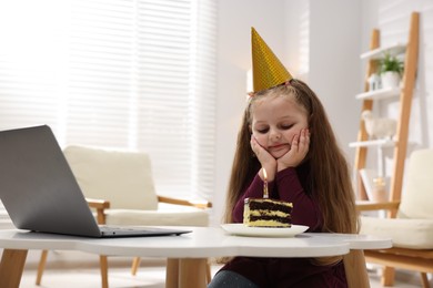 Photo of Birthday celebration. Little girl with piece of cake having video call via laptop at table indoors