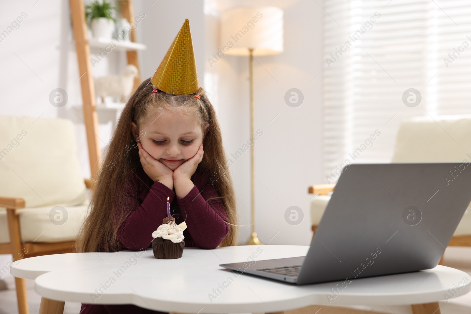 Birthday celebration. Little girl with cupcake having video call via laptop at table indoors Photo of Birthday celebration. Little girl with cupcake having video call via laptop at table indoors