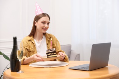 Photo of Birthday celebration. Happy woman with piece of cake having video call via laptop at home