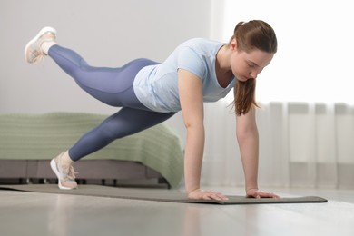Photo of Woman in sportswear doing plank exercise at home