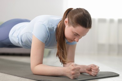 Photo of Woman in sportswear doing plank exercise at home