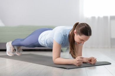 Photo of Woman in sportswear doing plank exercise at home