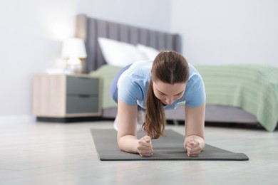 Photo of Woman in sportswear doing plank exercise at home, space for text