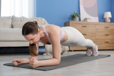 Photo of Woman in sportswear doing plank exercise at home