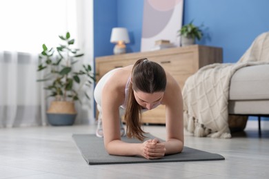 Photo of Woman in sportswear doing plank exercise at home