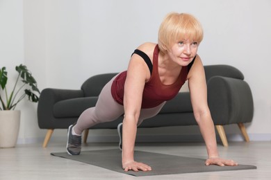 Photo of Senior woman in sportswear doing plank exercise at home, space for text