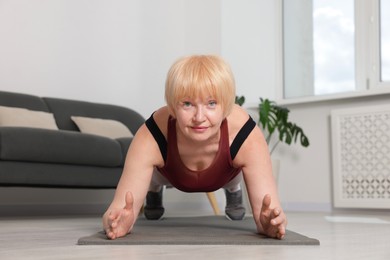 Photo of Senior woman in sportswear doing plank exercise at home