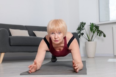 Photo of Senior woman in sportswear doing plank exercise at home