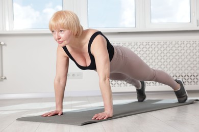 Photo of Senior woman in sportswear doing plank exercise at home