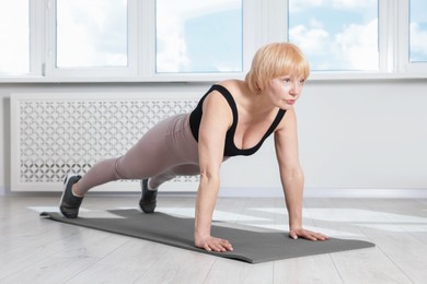 Photo of Senior woman in sportswear doing plank exercise at home