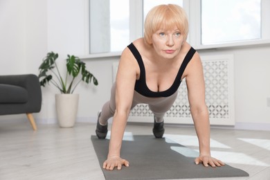 Photo of Senior woman in sportswear doing plank exercise at home, space for text