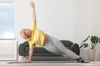 Photo of Senior woman in sportswear doing plank exercise at home