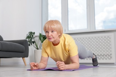 Photo of Senior woman in sportswear doing plank exercise at home