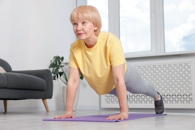Photo of Senior woman in sportswear doing plank exercise at home