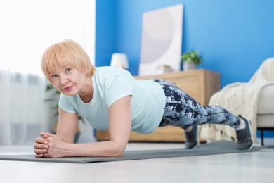 Photo of Senior woman in sportswear doing plank exercise at home
