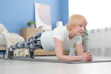 Photo of Senior woman in sportswear doing plank exercise at home