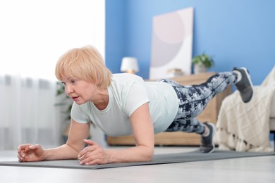 Photo of Senior woman in sportswear doing plank exercise at home