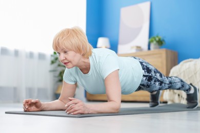 Photo of Senior woman in sportswear doing plank exercise at home