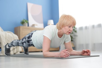 Photo of Senior woman in sportswear doing plank exercise at home